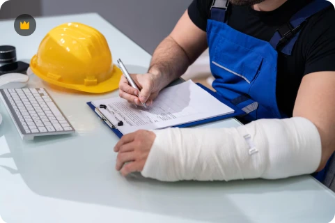 Construction worker in blue overalls with injured arm in white cast writing on clipboard at desk, yellow hard hat and keyboard visible - Types of Construction Estimation