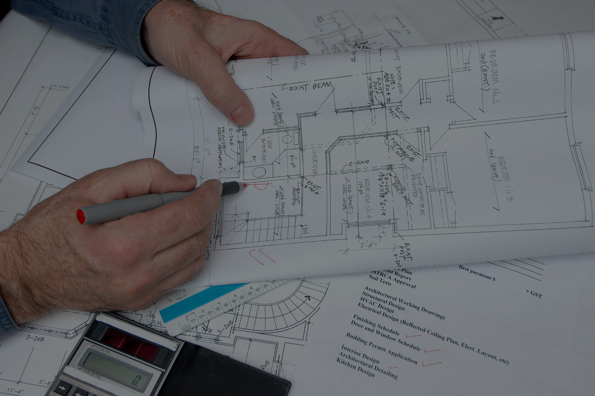 Architect marking construction blueprints with pen, calculator and architectural tools on table