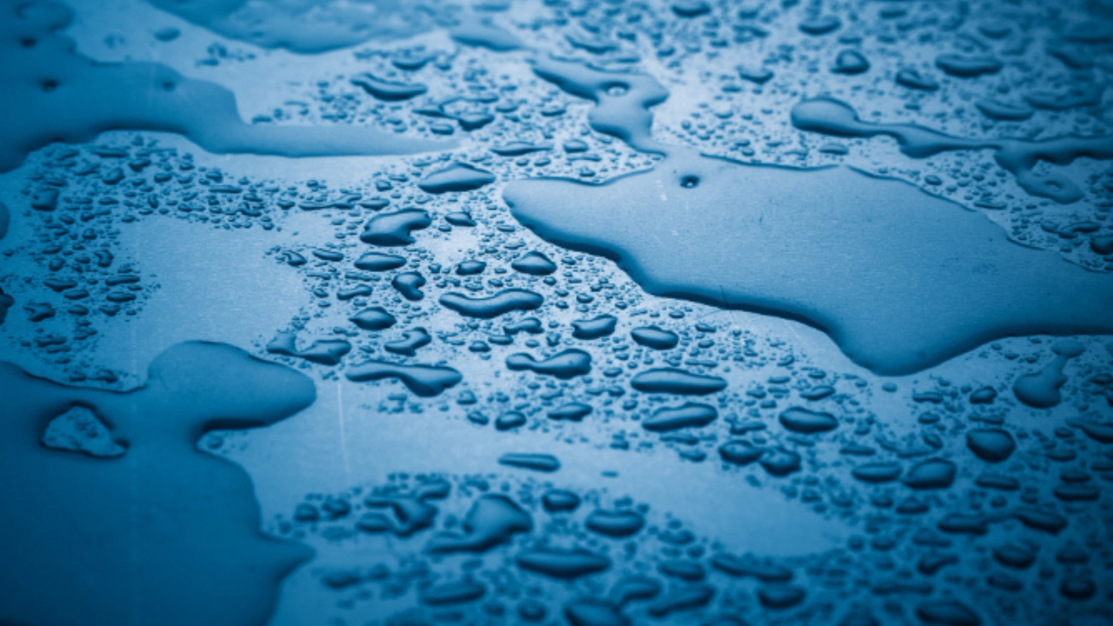 Close-up macro view of water droplets beading on blue surface showing surface tension