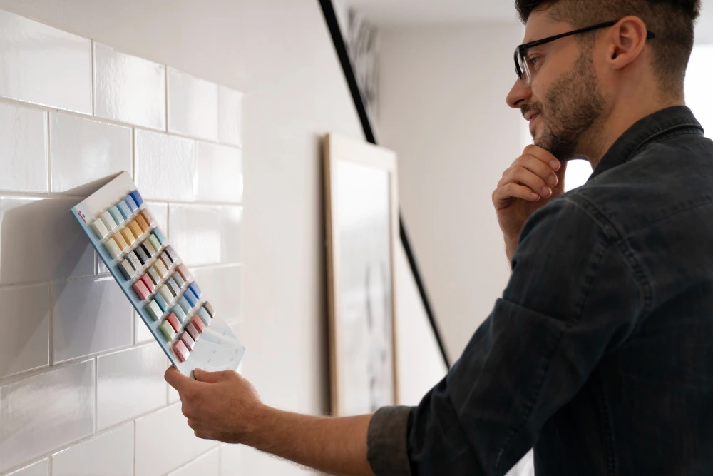Estimation expert in casual shirt examining colorful paint sample chart against white subway tile wall, choosing colors for interior design project