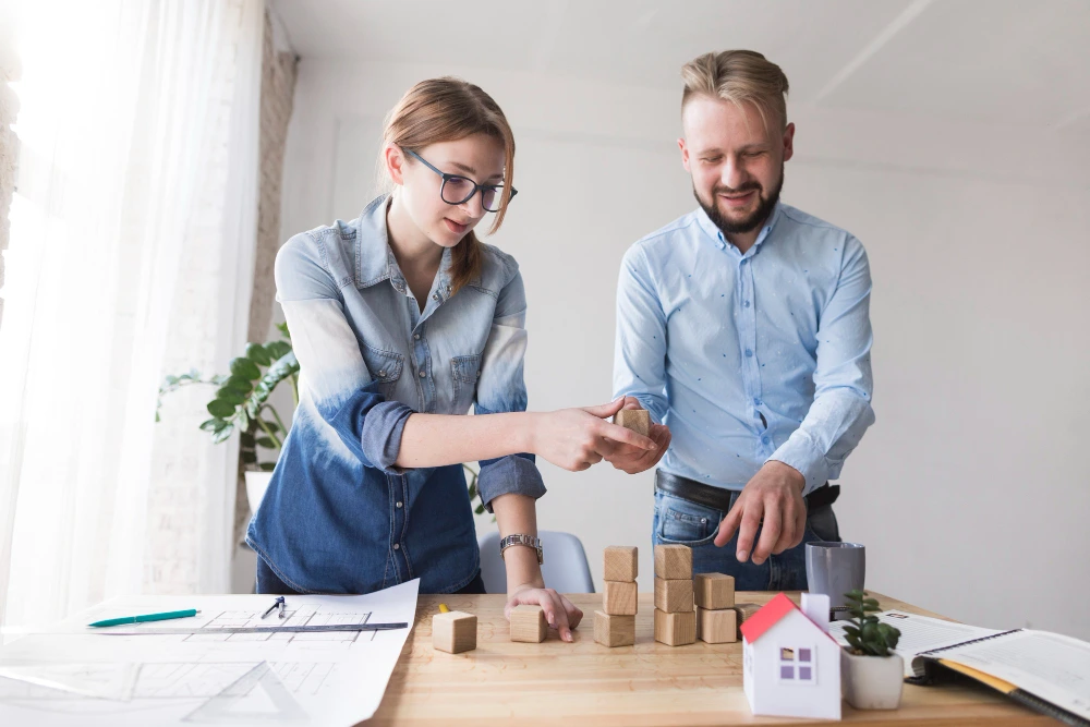 Construction professionals using wooden blocks and house model to demonstrate construction estimation concepts and project planning techniques