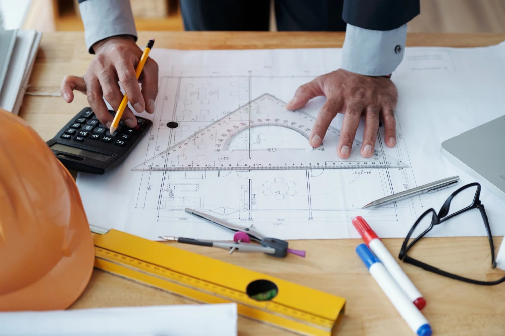Architect analyzing construction blueprints with calculator and drafting tools for CPM scheduling and project planning- 6 CPM Mistakes to Win More Bids