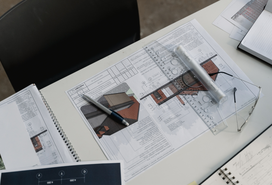 op view of construction plans on a desk, featuring architectural drawings, a pen, and a ruler for accurate measurements